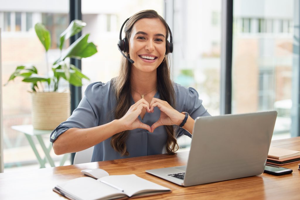 Woman, call center and laptop with heart gesture for telemarketing, customer service or support at the office. Portrait of happy employee consultant with smile and hands with love symbol by computer, digitale Gesundheit am Arbeitsplatz